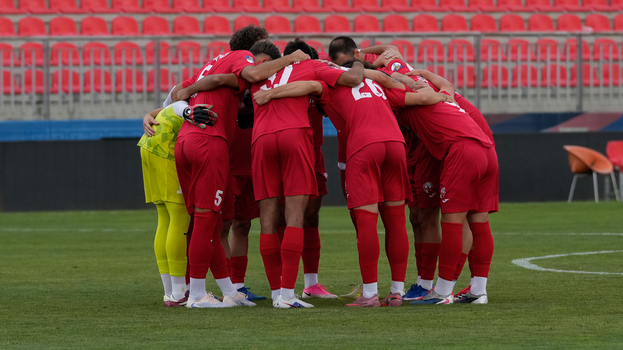 Fudbaleri Voždovca u crvenim dresovima u zagrljaju na terenu pre početka utakmice