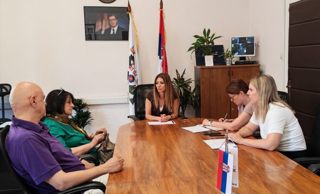 Predsednica opštine Voždovac Bojana Jakšić za stolom razgovara sa građanima, u pozadini zastave Srbije