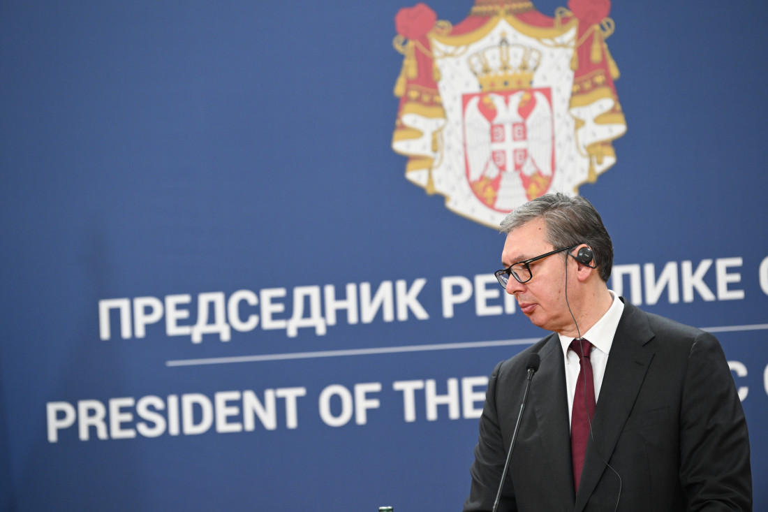Predsednik Srbije Aleksandar Vučić za govornicom ispred plave pozadine sa grbom Republike Srbije