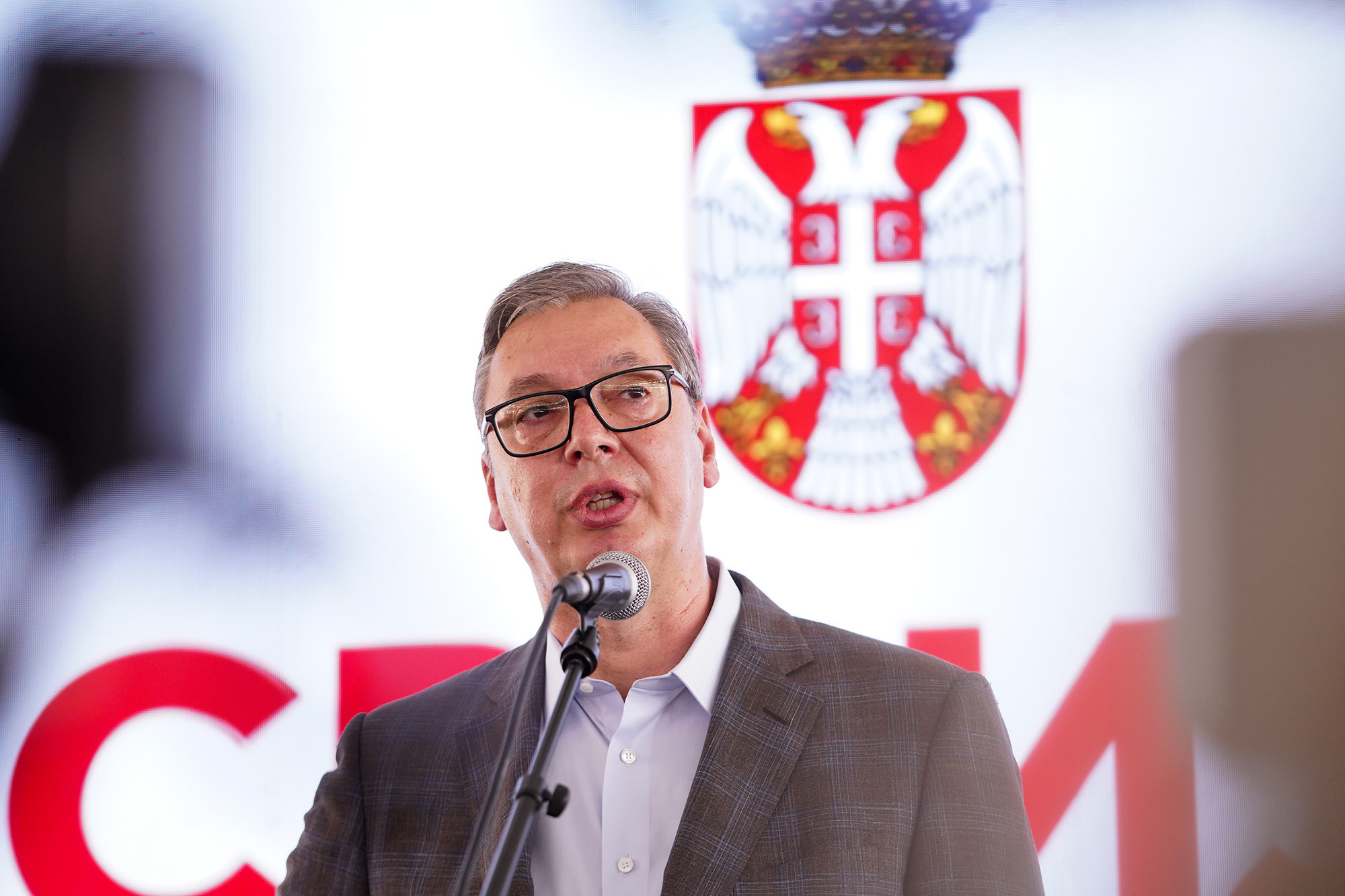 Predsednik Aleksandar Vučić govori za mikrofonom ispred grba Srbije