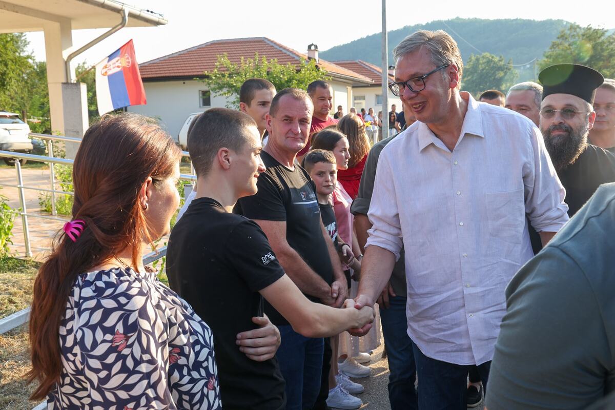 Aleksandar Vučić se rukuje sa mladićem ispred kuće, okupljeni meštani i srpska zastava u pozadini