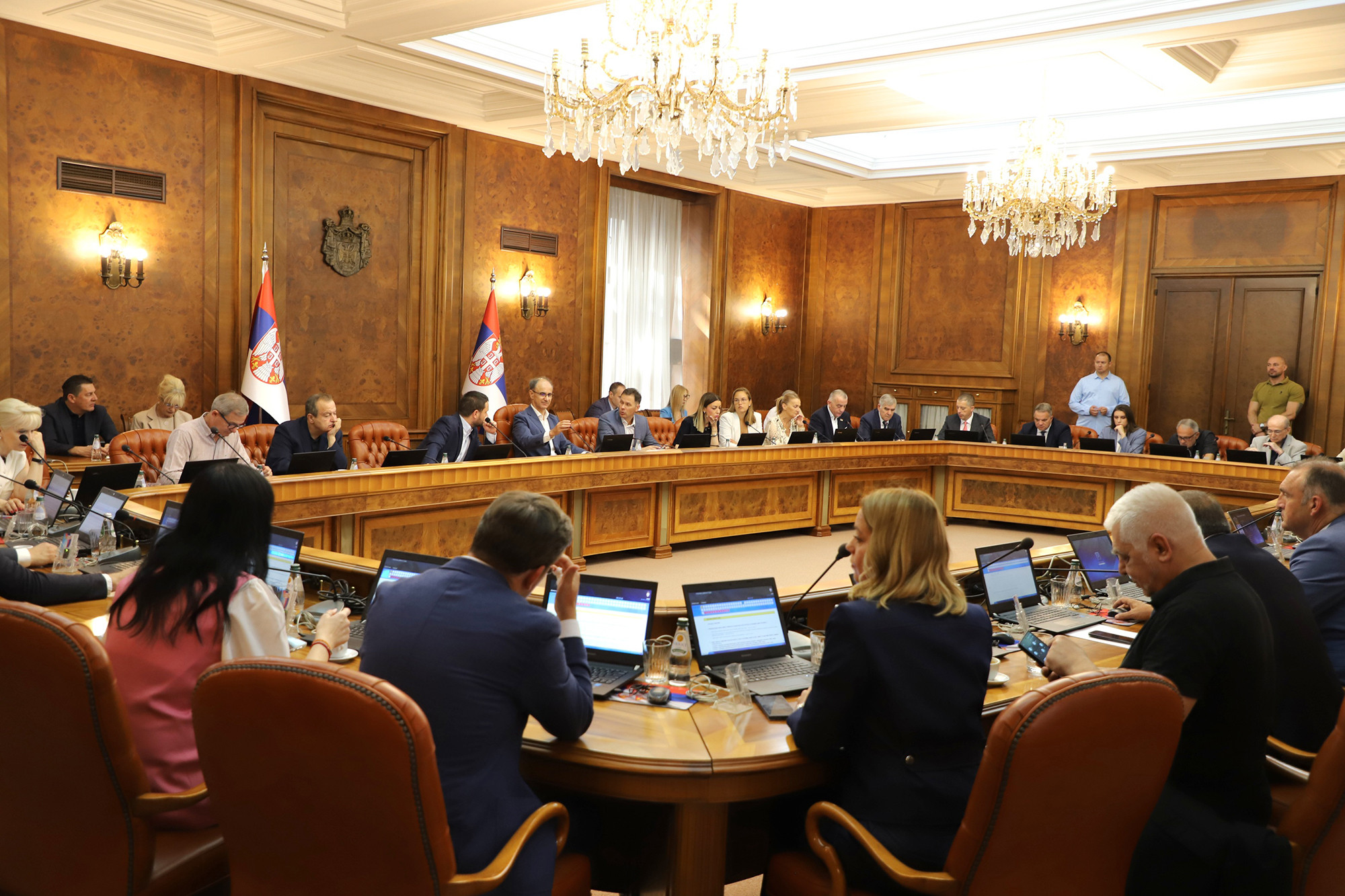 Sednica Vlade Srbije, članovi vlade za velikim stolom u sali sa lusterima i zastavama Srbije
