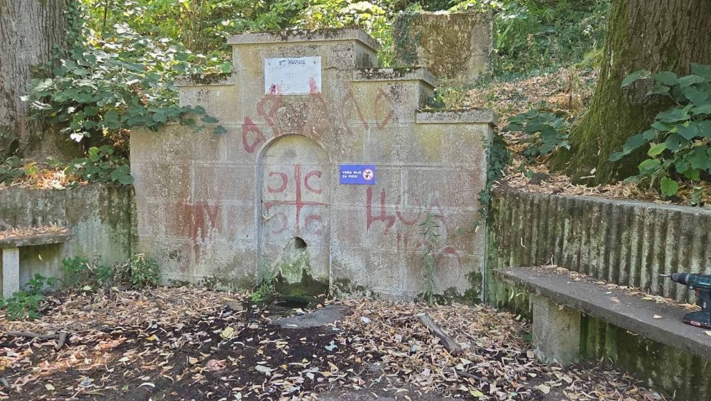 Stara kamena česma u šumi sa plavom tablom na kojoj piše da voda nije za piće