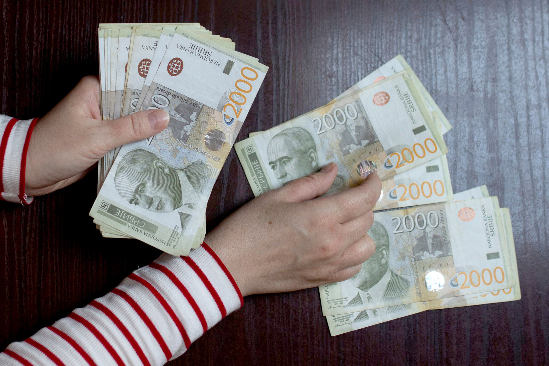 Ruke broje novčanice od 2.000 dinara na tamnom stolu