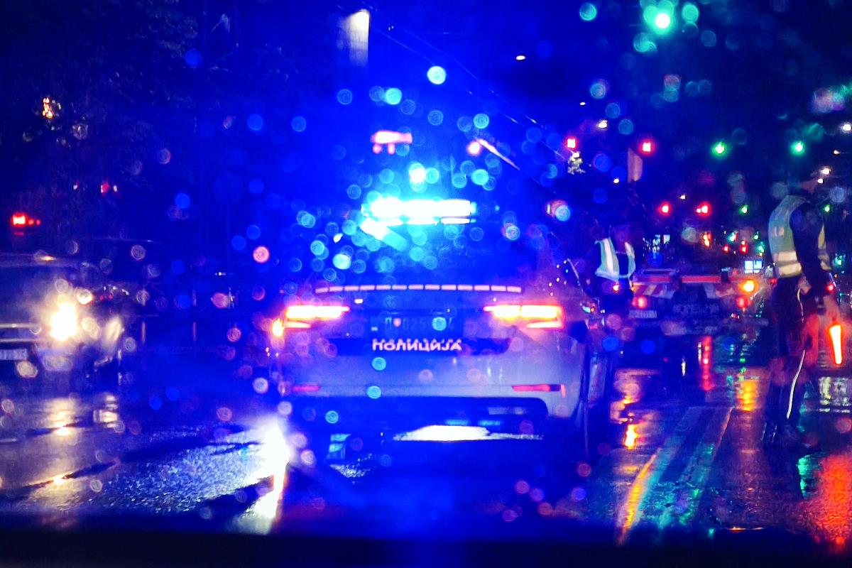 Policijski automobil sa upaljenim rotacionim svetlima na mokrom kolovozu noću