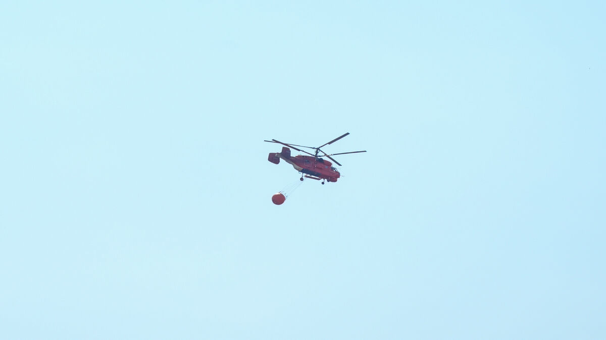 Crveni protivpožarni helikopter sa kantom za vodu leti iznad zadimljenog neba