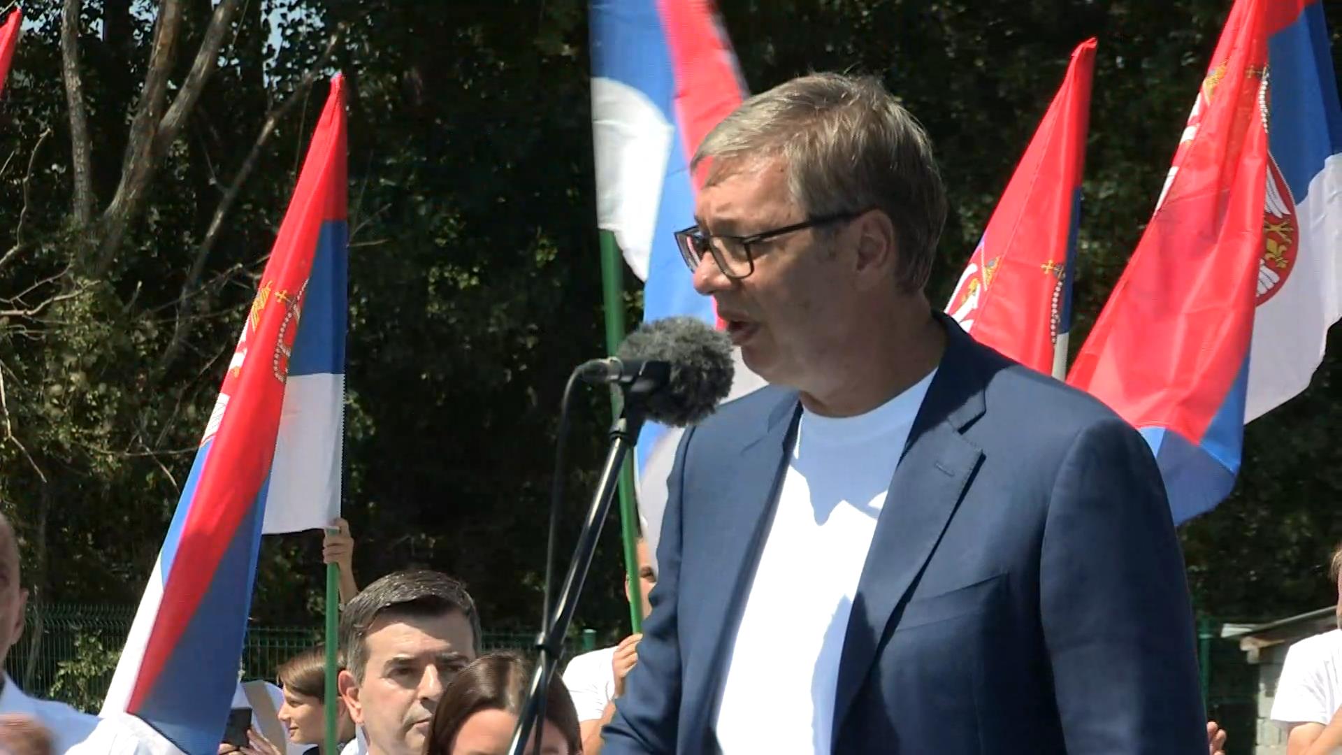 Aleksandar Vučić govori ispred mikrofona, iza njega građani sa srpskim zastavama
