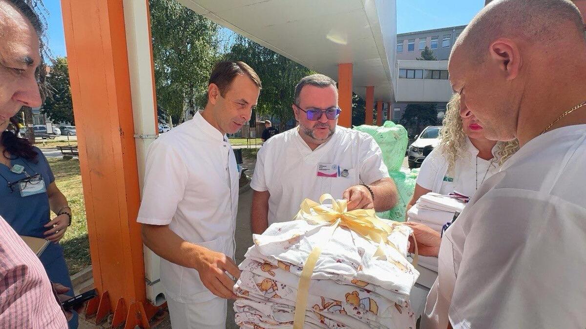 Lekari u belim mantilima drže složene komplete posteljine ispred zgrade porodilišta
