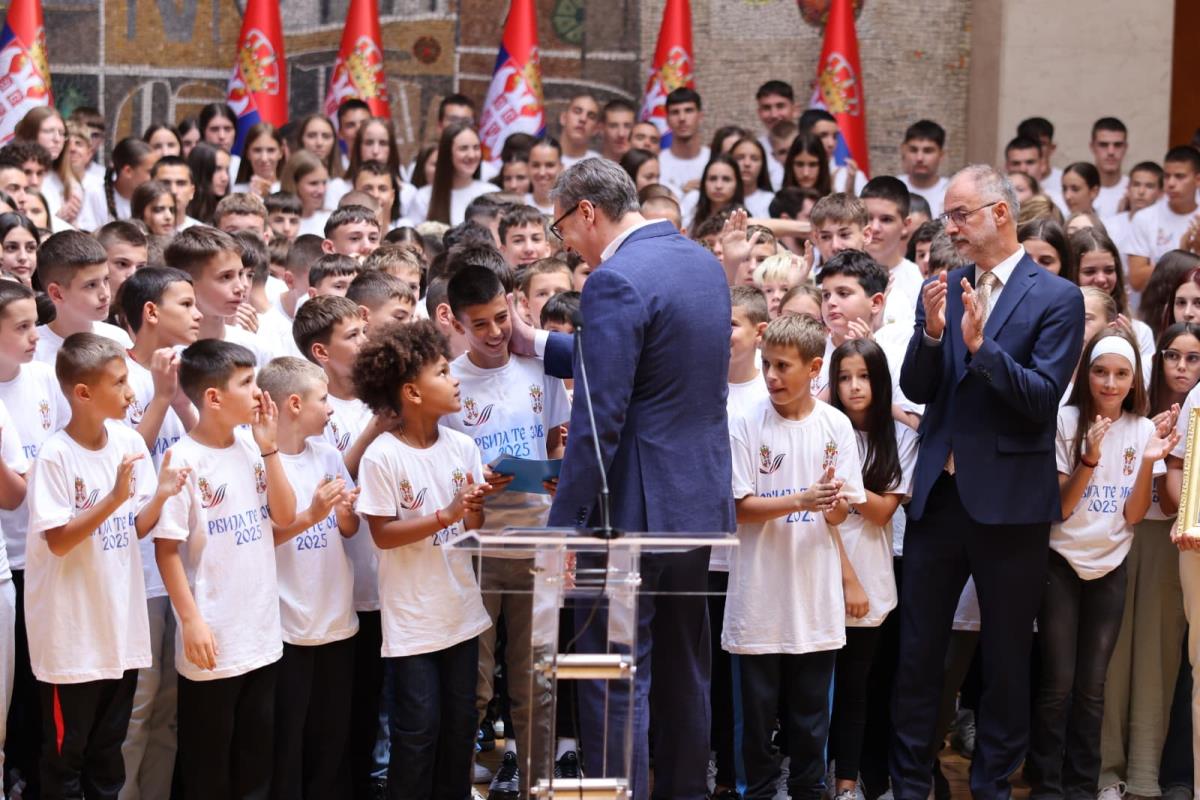 Predsednik Srbije govori pred decom u belim majicama kampa Srbija te zove, u pozadini zastave Srbije