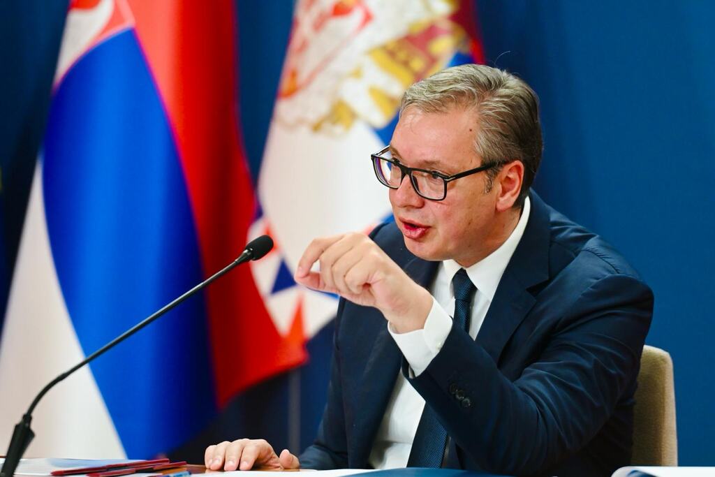 Aleksandar Vučić govori za stolom, iza njega zastave Srbije