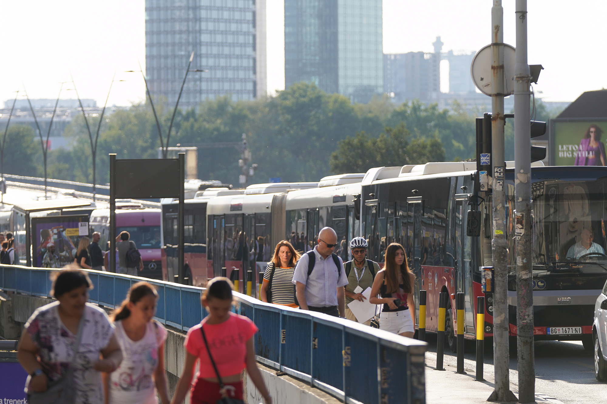 Prolaznici u letnjoj odeći na beogradskoj ulici pored kolone autobusa, po vrelom danu