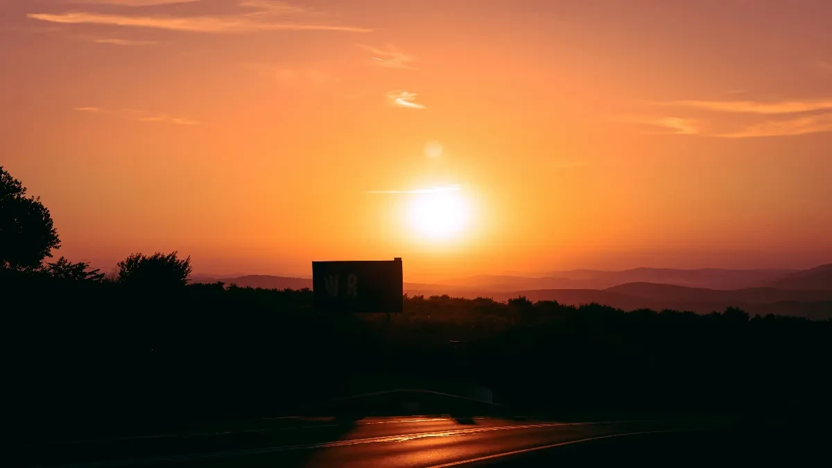 Užareno narandžasto sunce nisko nad horizontom iznad puta i brda u sumrak