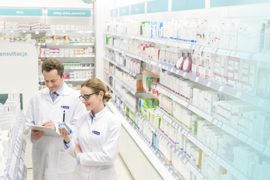 Dvoje farmaceuta u belim mantilima pored polica sa lekovima u apoteci