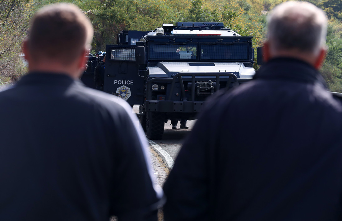 Oklopno vozilo kosovske policije na putu, dvojica muškaraca posmatraju u prvom planu