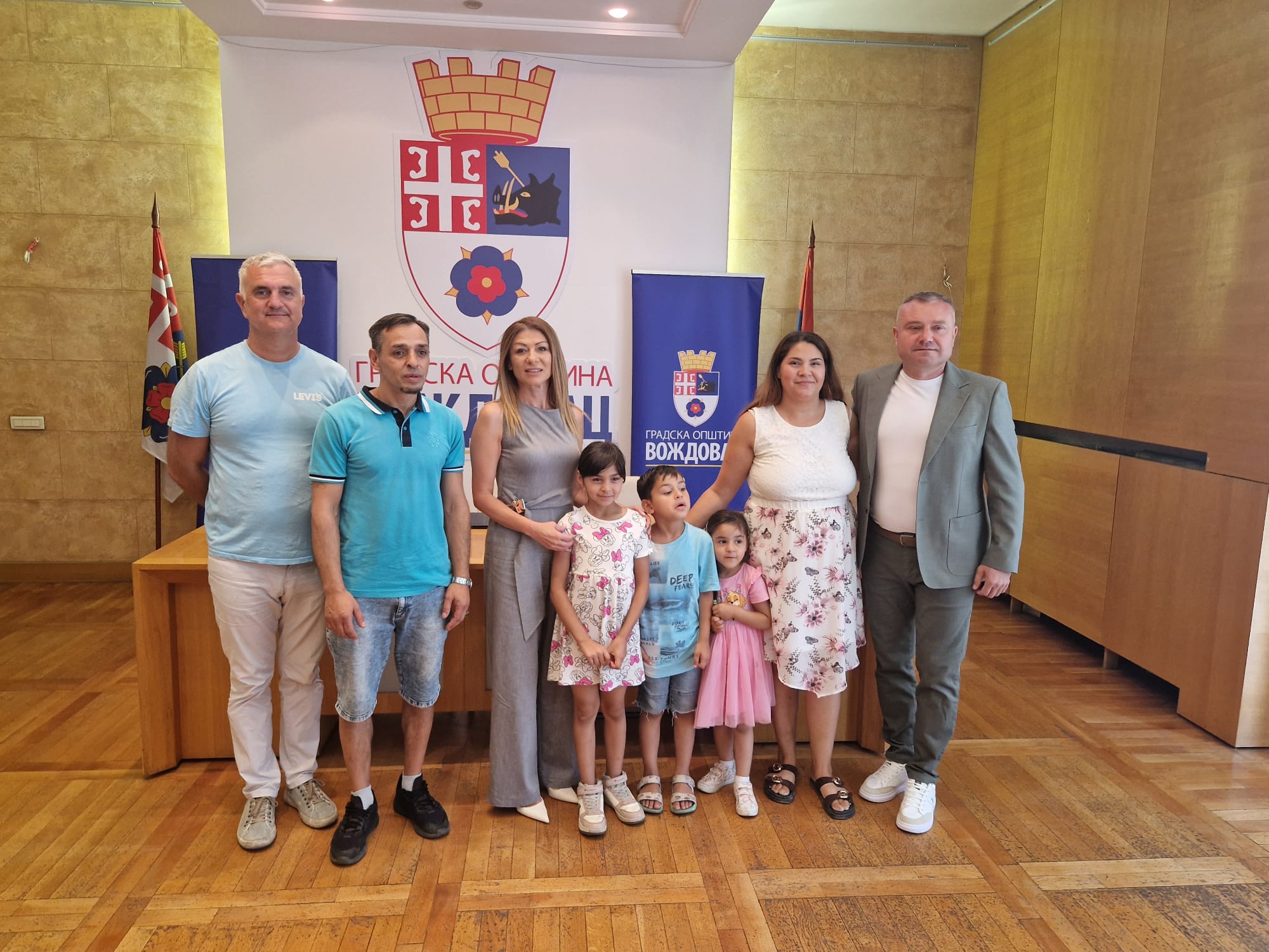 Porodica sa troje dece i opštinski funkcioneri poziraju u svečanoj sali ispred grba i banera Gradske opštine Voždovac