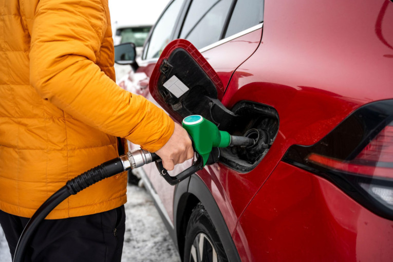 Osoba u žutoj jakni toči gorivo zelenim pištoljem u crveni automobil