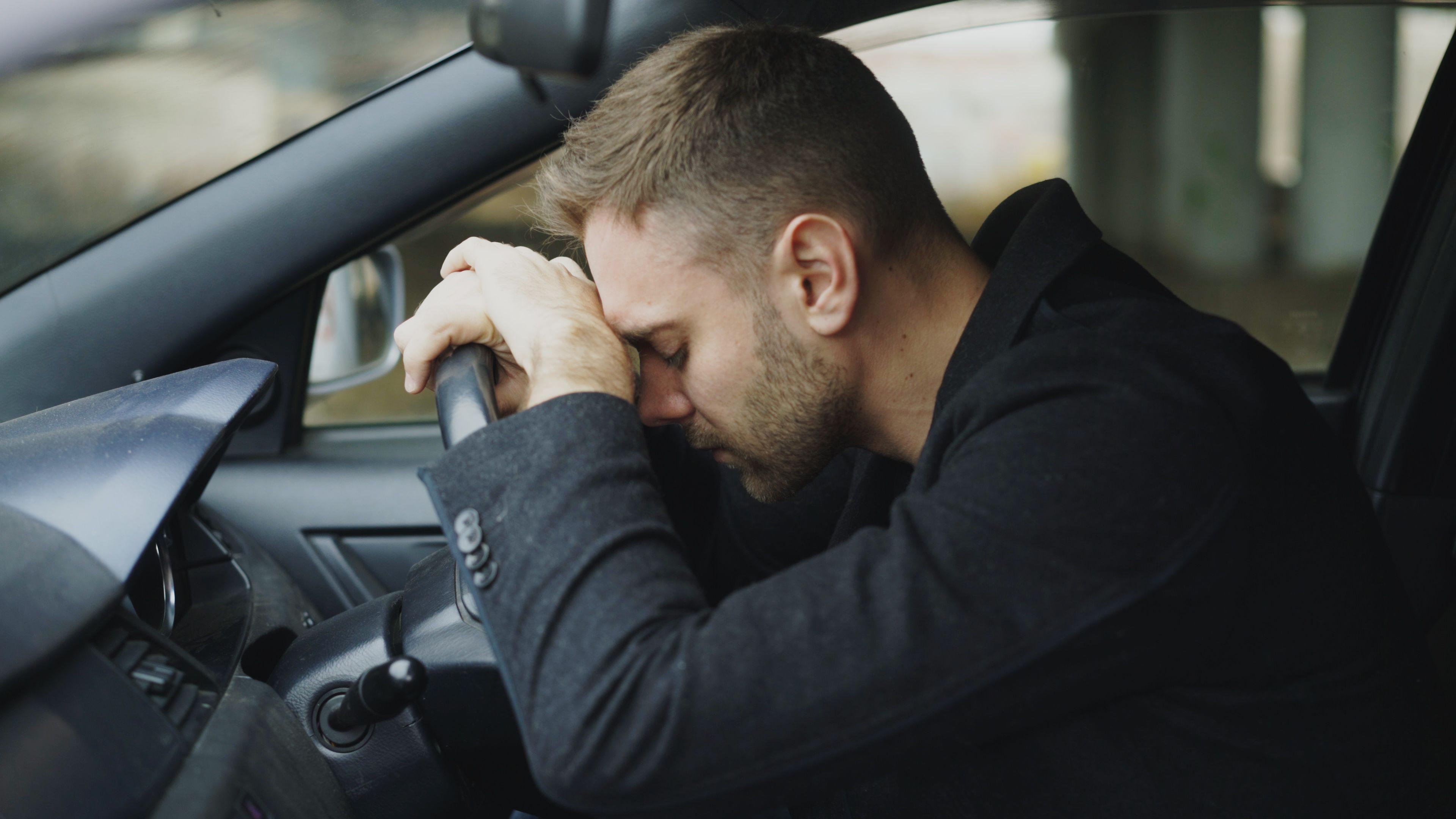Muškarac naslonjen čelom na volan u automobilu