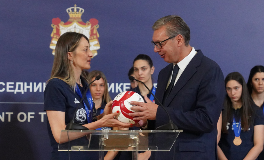 Maja Ognjenović uručuje Aleksandru Vučiću potpisanu odbojkašku loptu, iza njih reprezentativke sa medaljama