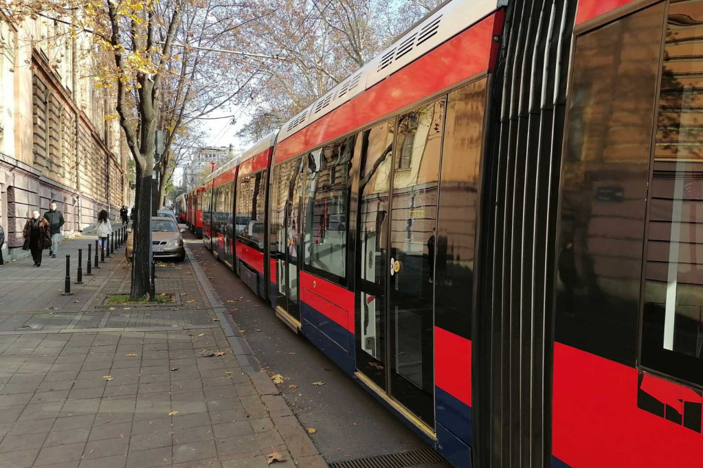 Crveno-beli tramvaj u beogradskoj ulici pored trotoara