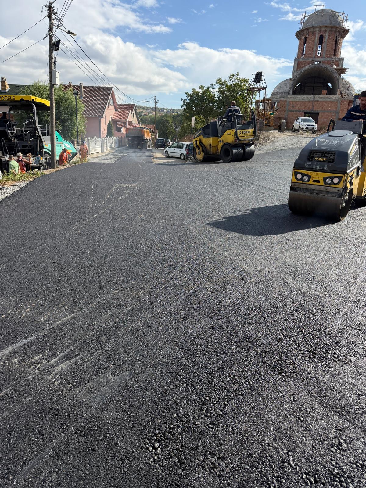 Sveže asfaltirana ulica sa valjcima i finišerom, u pozadini hram u izgradnji
