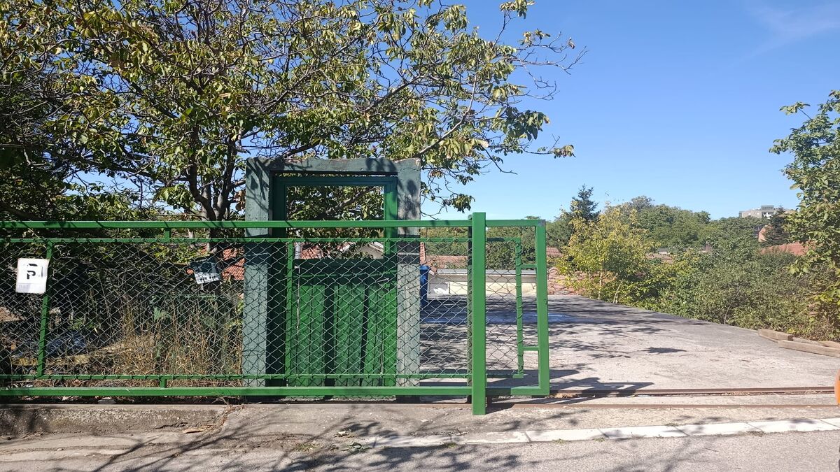 Zelena metalna kapija i ograda dvorišta kuće, u pozadini drveće i krovovi