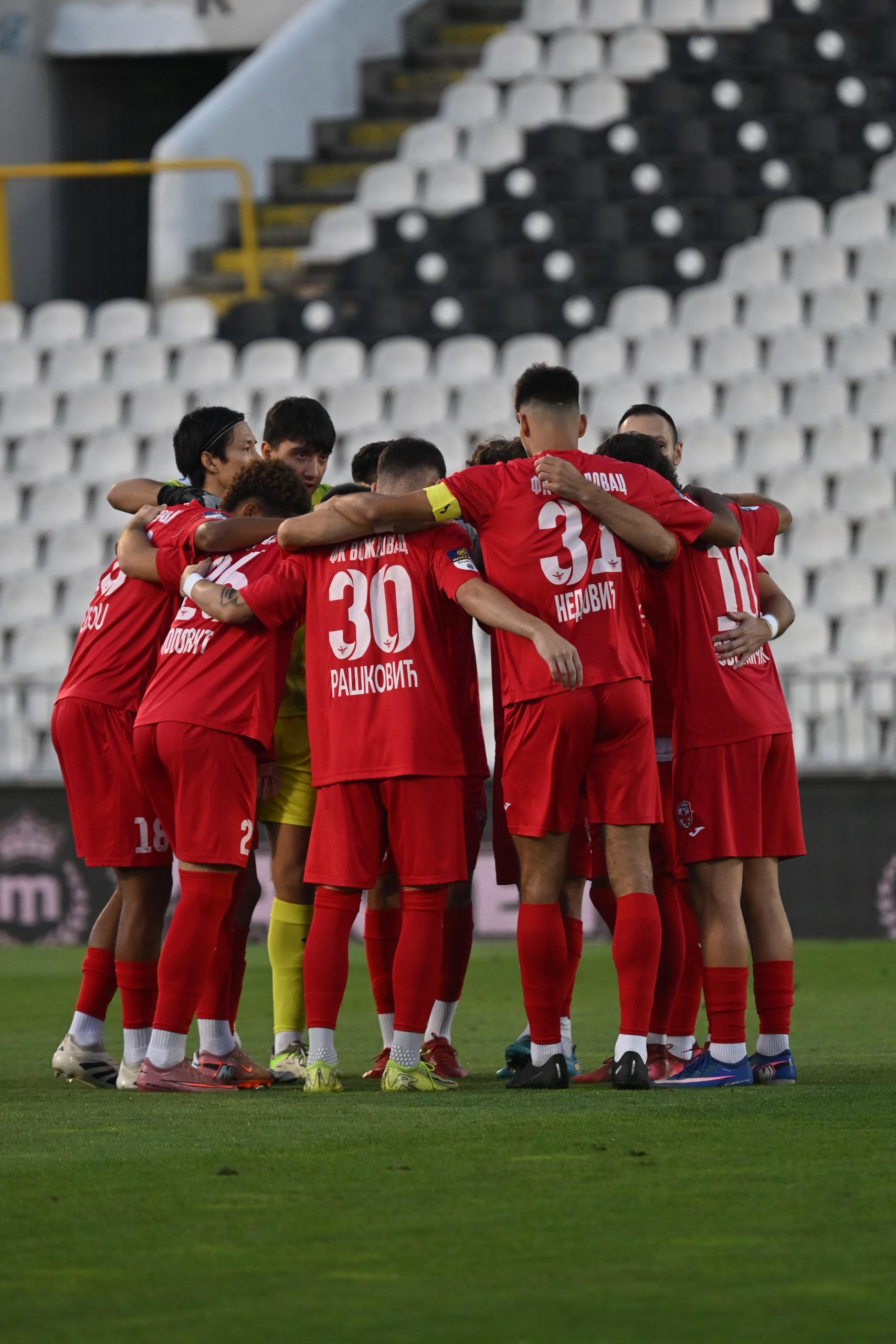 Fudbaleri Voždovca u crvenim dresovima okupljeni u krugu na terenu pred utakmicu