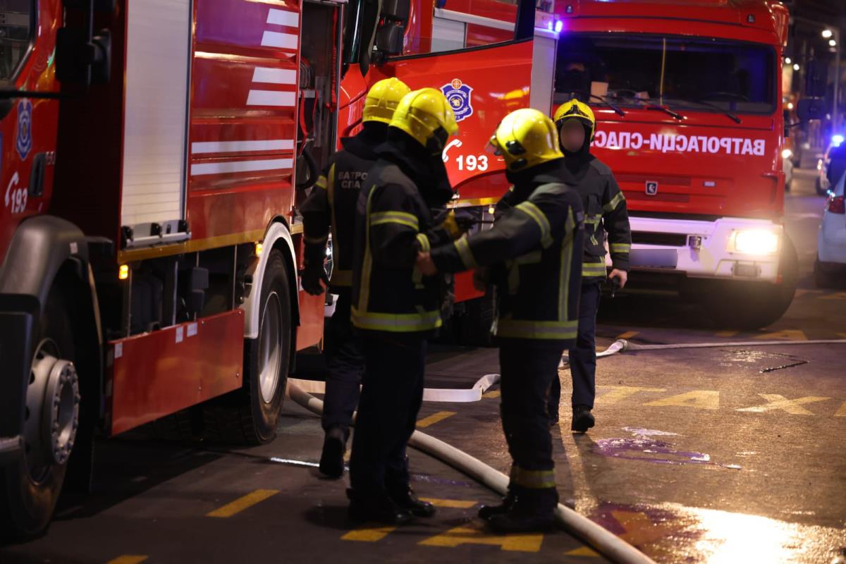 Vatrogasci sa žutim šlemovima stoje pored vatrogasnih vozila noću