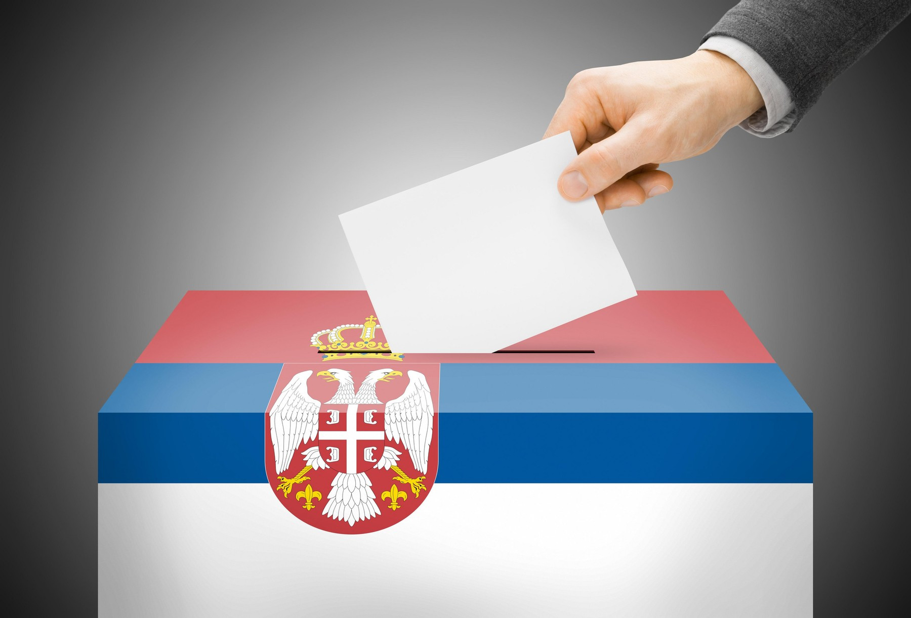 Ruka ubacuje glasački listić u glasačku kutiju u bojama zastave Srbije