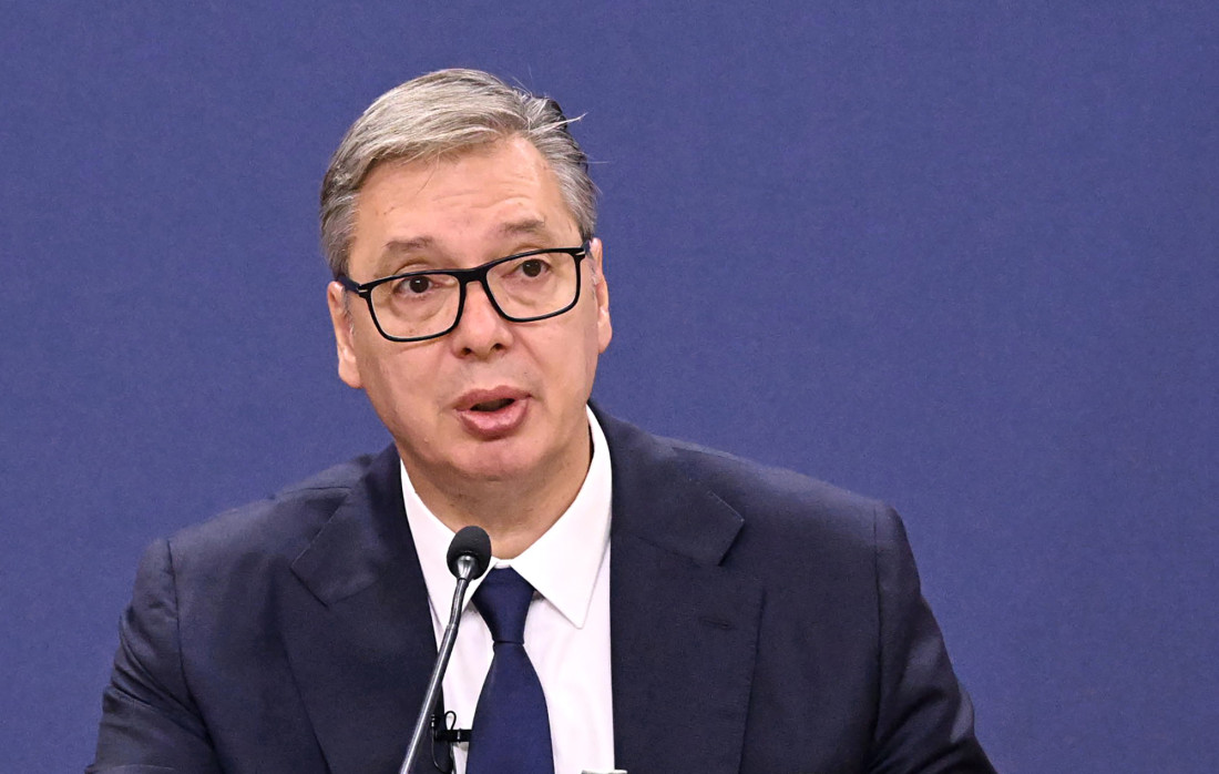 Aleksandar Vučić u tamnom odelu sa naočarima govori za govornicom ispred plave pozadine