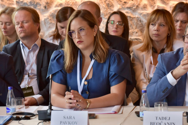 Sara Pavkov sedi za konferencijskim stolom sa pločicom sa svojim imenom, okružena učesnicima sastanka