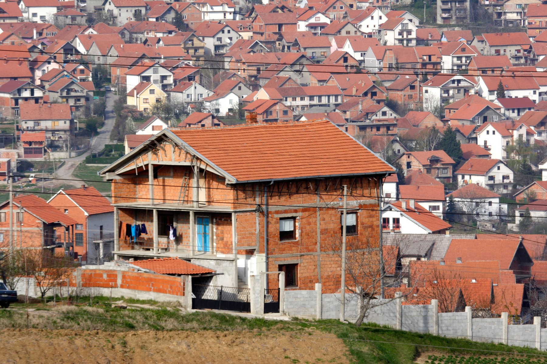 Nedovršena kuća od cigle ispred naselja sa kućama crvenih krovova