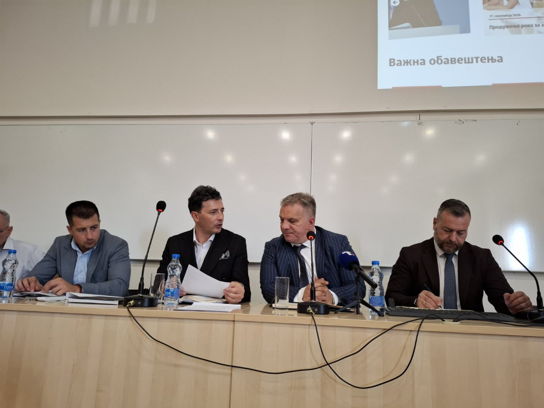 Učesnici sastanka za stolom sa mikrofonima u sali