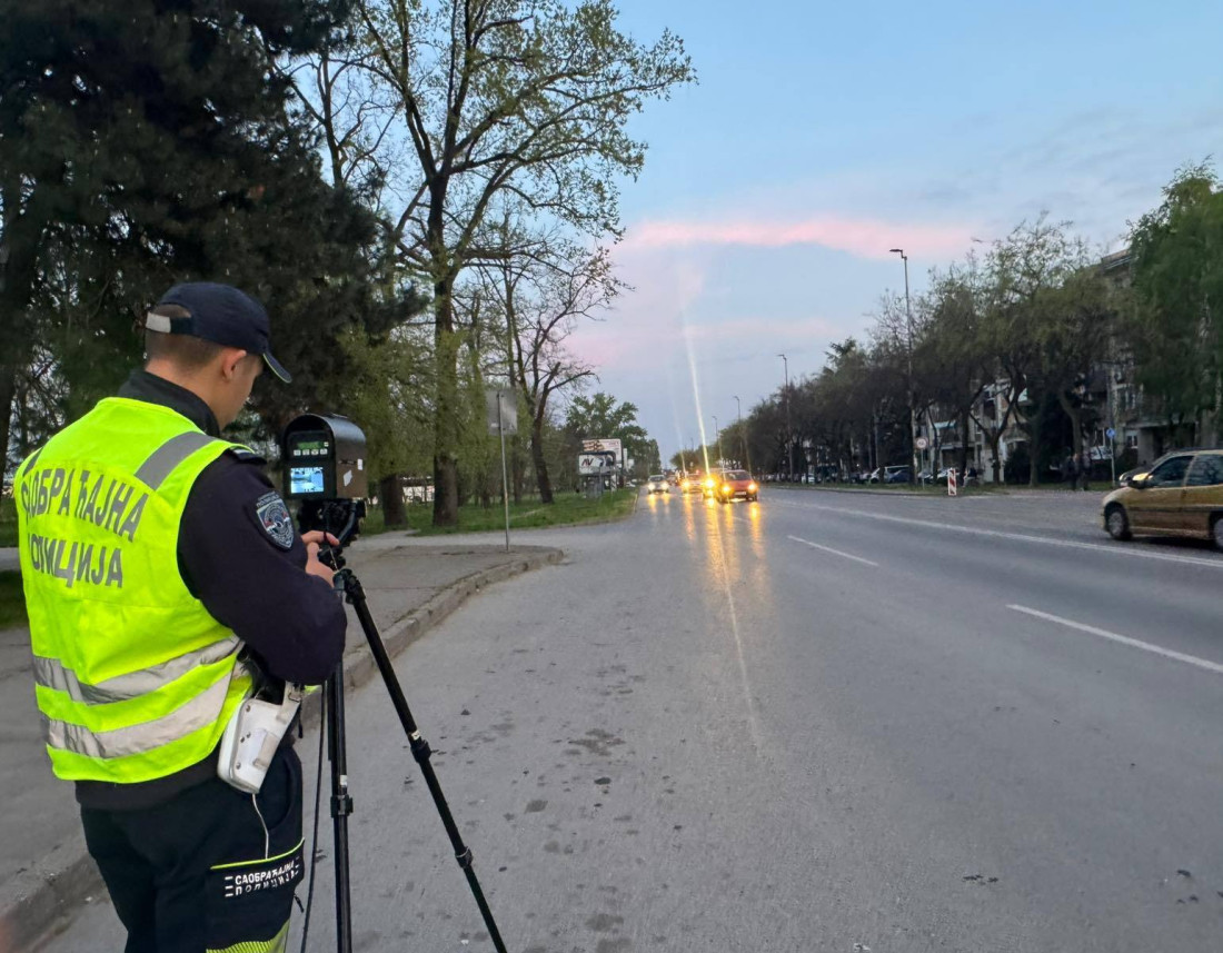 Pripadnik saobraćajne policije u prsluku sa radarom pored bulevara u sumrak