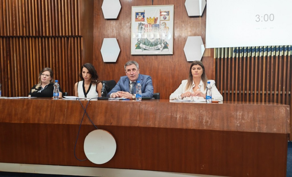 Predsedavajući i saradnici za stolom u skupštinskoj sali GO Voždovac, iznad njih grb opštine