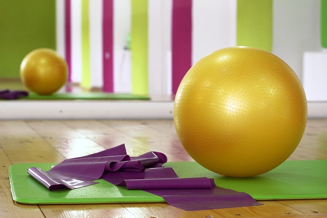 Žuta pilates lopta, elastična traka i zelena prostirka na parketu u sali za vežbanje