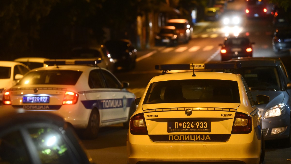 Dva policijska automobila noću na ulici sa upaljenim svetlima