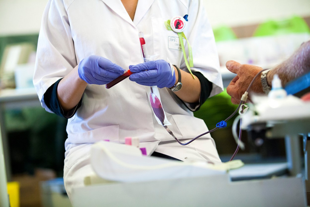 Medicinska radnica u rukavicama drži epruvetu sa krvlju tokom davanja krvi