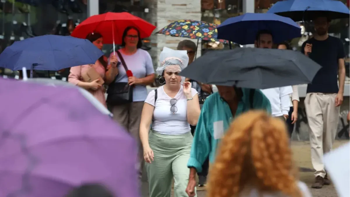 Prolaznici sa kišobranima na gradskoj ulici tokom kiše