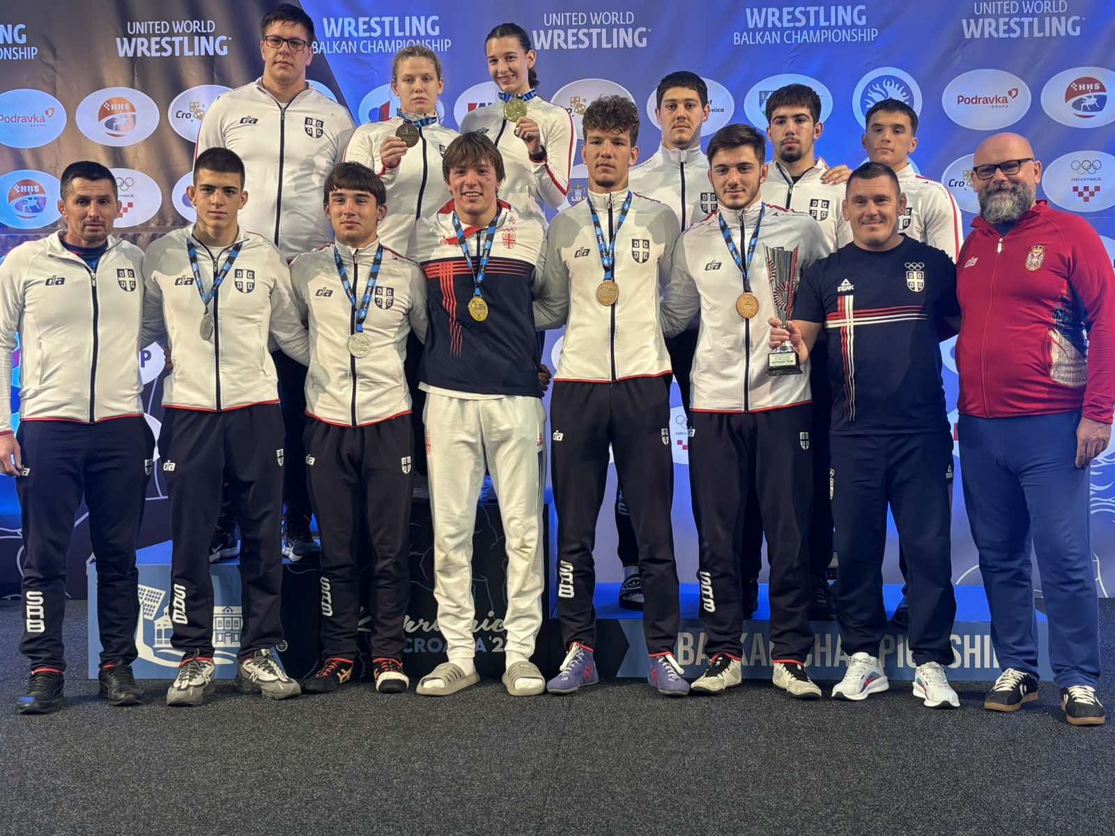 Mladi rvači i stručni štab reprezentacije Srbije sa medaljama i peharom ispred panoa Balkanskog šampionata
