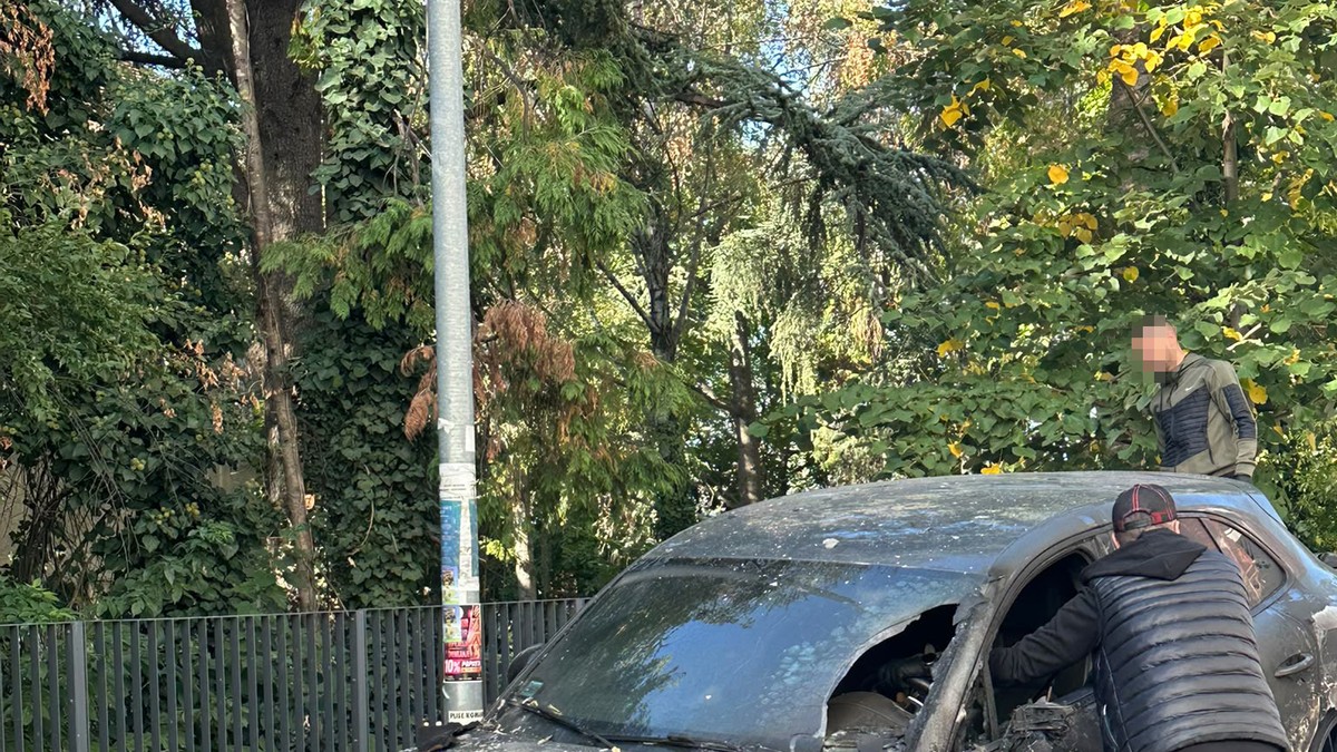 Izgoreli automobil parkiran uz ogradu, muškarac pregleda unutrašnjost vozila