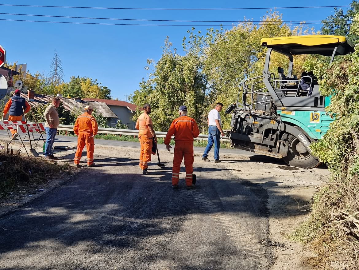 Radnici u narandžastim kombinezonima i finišer za asfalt na ulici tokom radova