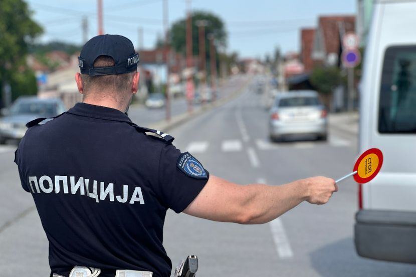 Saobraćajni policajac u uniformi sa natpisom Policija zaustavlja vozilo saobraćajnom palicom