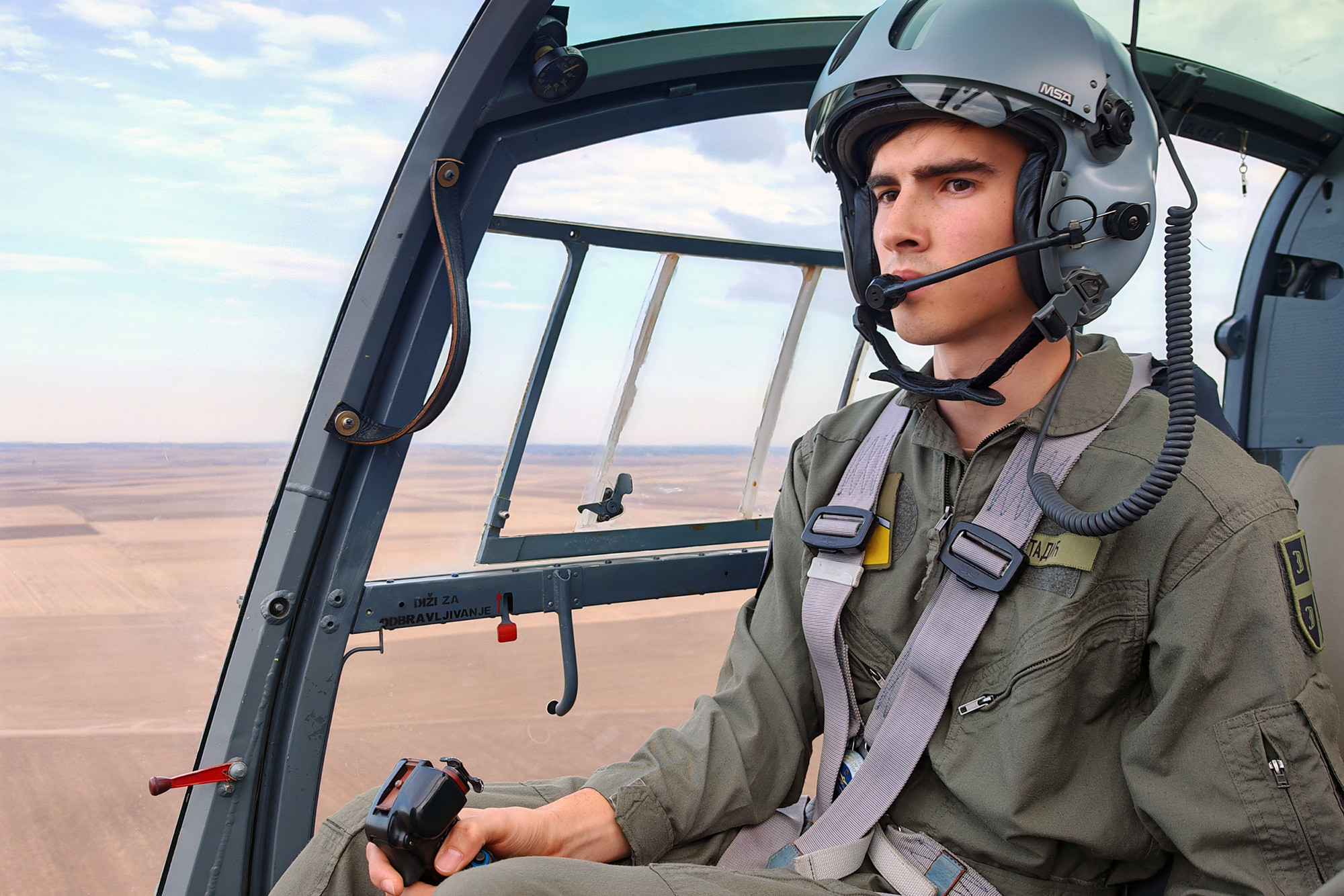 Kadet u pilotskoj kacigi za komandama helikoptera tokom leta iznad ravnice