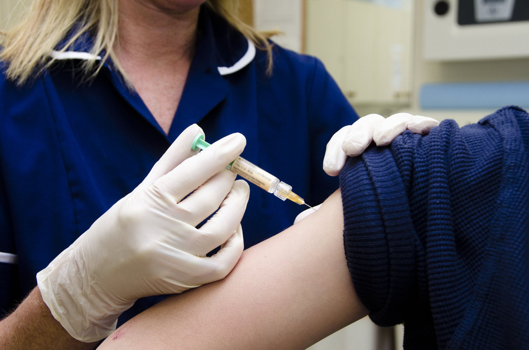 Medicinska sestra u plavoj uniformi daje injekciju u nadlakticu pacijenta