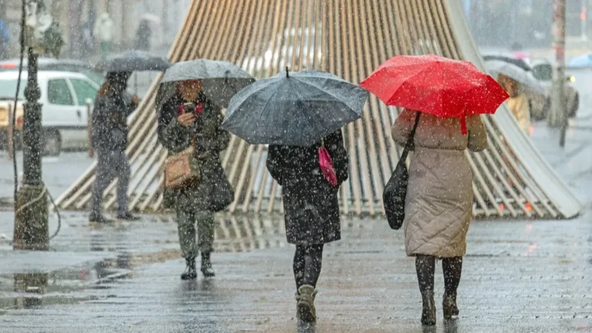 Prolaznici sa kišobranima na gradskoj ulici tokom susnežice