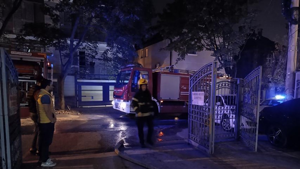 Vatrogasno vozilo i vatrogasac ispred kapije zgrade u noćnim satima