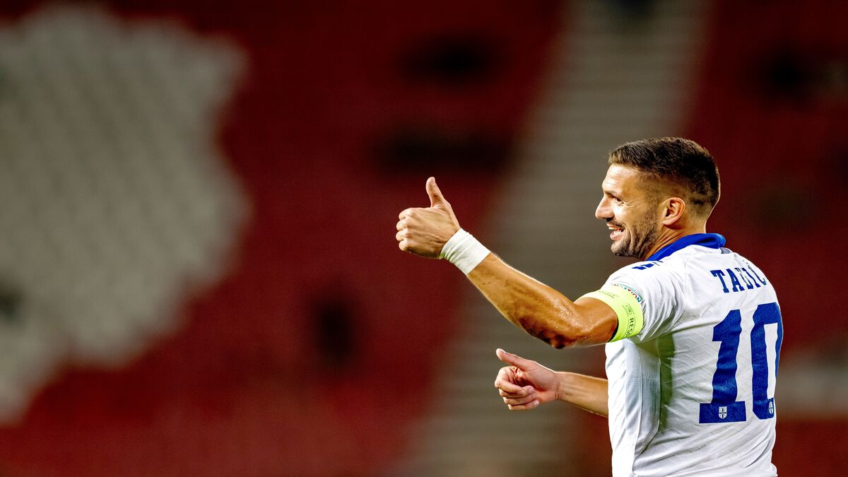Dušan Tadić u belom dresu reprezentacije Srbije sa brojem 10 pokazuje palac gore, u pozadini crvene tribine stadiona