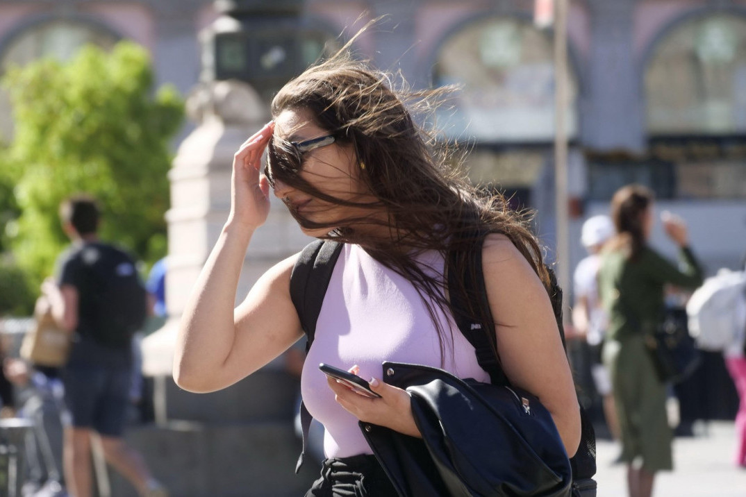 Žena sa sunčanim naočarima na suncu u gradu, vetar joj nosi kosu